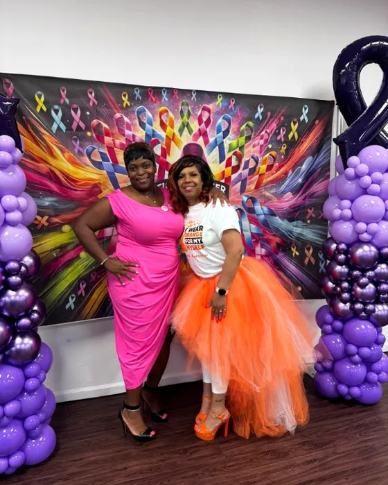 Two supporters together in front of a wall of awareness ribbons at a Colors of Warriors event
