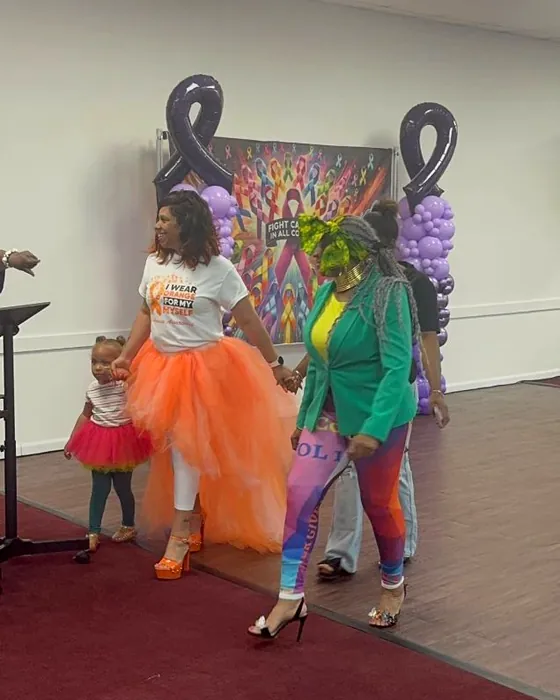 Supporters walking the runway in orange at an awareness event, a small child walking with them